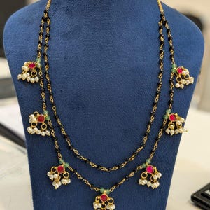 May include: A gold-toned necklace with two strands of black beads. The necklace features red and white accents, with small pearls and green beads. The text "FW75" is visible in the upper right corner.