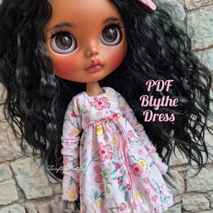 May include: A Blythe doll with long black hair and a pink flower hair clip. The doll wears a pink floral dress with long sleeves and a lace hem. The text "PDF Blythe Dress" is visible.