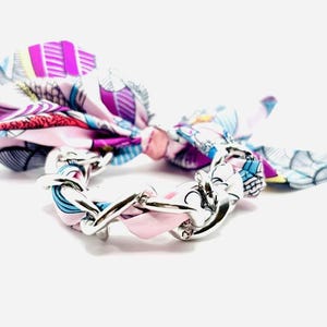 May include: A colorful silk scarf tied around a silver chain bracelet. The scarf features a pattern of pink, purple, blue, and white designs. The bracelet is made of interlocking silver links.