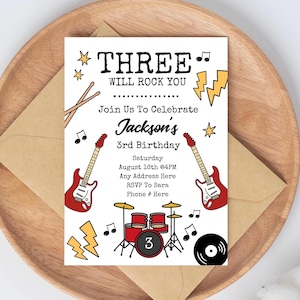 以下が含まれることがあります： ロックンロールをテーマにした誕生日招待状。「THREE WILL ROCK YOU」というテキストと、ギター、ドラム、音符のイラストが特徴です。招待状は白い背景にあります。
