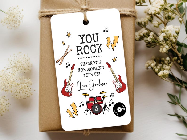 May include: A rectangular white gift tag featuring black text that reads YOU ROCK THANK YOU FOR JAMMING WITH US! and Love Jackson. The design includes illustrations of two red electric guitars, a red drum set with the number 3, lightning bolts, and music notes.