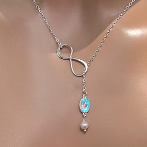 May include: A silver-toned lariat necklace featuring an infinity symbol and a dangling pendant. The pendant includes a natural moonstone and a small pearl. The necklace is displayed on a person.
