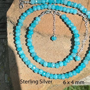 Könnte beinhalten: Ein Set aus drei Keramikbechern mit gesprenkelter, cremefarbener Glasur. Jeder Becher zeigt ein handgemaltes Design: ein grünes Blatt, eine blaue Blume und eine gelbe Sonne. Die Becher haben ein schlichtes, modernes Design.