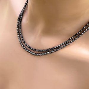 May include: A double strand necklace made of black pearls. The pearls are round and have a slight iridescent sheen.