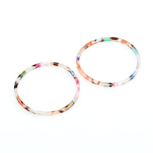 May include: Two colorful, round, plastic hair ties with a speckled pattern.
