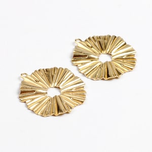 Peut inclure: Deux pièces décoratives en métal de couleur dorée de forme circulaire avec un design texturé et plissé. Les pièces ont un trou au centre et une petite boucle en haut.