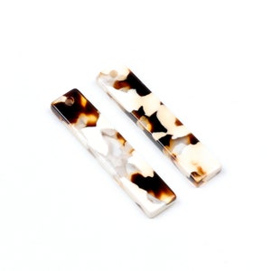 Puede incluir: Dos pinzas para el pelo rectangulares, de plástico, con estampado blanco y marrón, con un agujero en la parte superior.