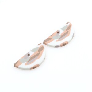 May include: Two half-circle shaped polymer clay earrings with a white base and a brown and gray abstract pattern.