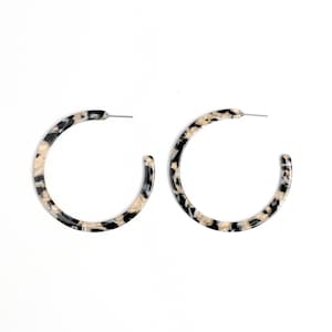 Peut inclure: Une paire de boucles d'oreilles créoles noires et crème avec un motif marbré.