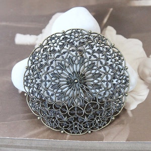 Puede incluir: Un gran medallón redondo decorativo de metal con un diseño de filigrana. El medallón está hecho de un metal oscuro de aspecto antiguo y tiene un patrón circular de detalles intrincados.
