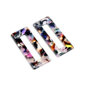Op de afbeelding: Twee rechthoekige haarclips met een kleurrijk, abstract patroon. De clips zijn gemaakt van een doorschijnend materiaal en hebben een rechthoekige opening in het midden.
