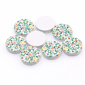May include: Eight round wooden discs with a white background and a floral pattern in shades of pink, green, and orange. The discs are arranged in a circle.