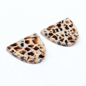 Puede incluir: Dos colgantes de resina en forma de semicírculo con un patrón moteado marrón y blanco.