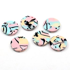 以下が含まれることがあります： 吊り下げ用の穴が付いた、丸いカラフルな模様の入ったアクリル製のチャームが6個。チャームは、ピンク、ブルー、イエロー、ブラックの色が渦巻き状に抽象的なデザインで混ざり合っています。