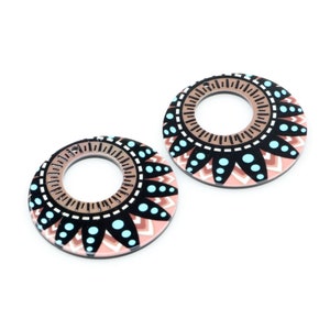 May include: A pair of large, round earrings with a geometric design. The earrings are painted in shades of pink, brown, black, and turquoise.