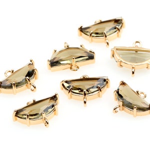 May include: Seven gold-toned metal half-circle charms with clear green glass stones. Each charm has a loop at the top and three prongs at the bottom.