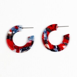 May include: A pair of red, white and blue hoop earrings. The earrings are made from a marbled plastic material.