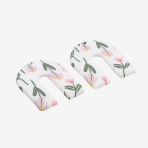 Könnte beinhalten: Zwei weiße, bogenförmige Ohrringe aus Polymer Clay mit einem Blumenmuster. Das Muster zeigt rosa Blüten und grüne Blätter.