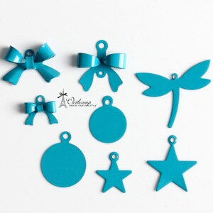 May include: Assortment of turquoise blue metal charms in various shapes, including bows, stars, circles, and a dragonfly. The charms have a hole at the top for attaching to jewelry or other crafts.