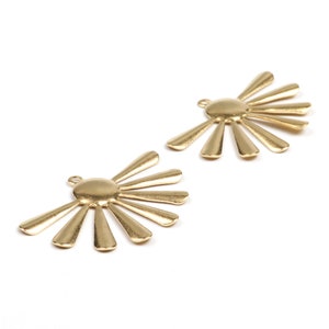 Könnte beinhalten: Zwei goldene Sonnenstrahlen-Anhänger aus Metall mit einem runden Zentrum und strahlenden Punkten. Die Anhänger haben oben ein Loch zum Anbringen an Schmuck oder andere Bastelarbeiten.