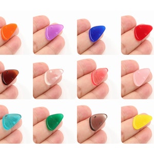 Op de afbeelding: Twaalf driehoekige gitaarplectrums in verschillende kleuren, waaronder oranje, paars, blauw, rood, bruin, transparant, groen en geel.