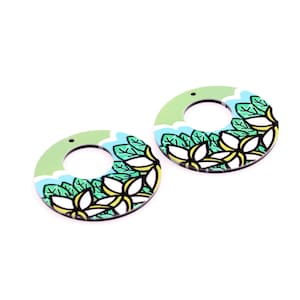May include: A pair of circular earrings with a floral design. The earrings have a light green border with a blue and white wave pattern. The centre of the earrings features a white flower with yellow accents and green leaves. Each earring has a small hole at the top.
