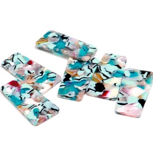 May include: Six rectangular turquoise, white, black, and pink patterned acrylic resin beads. The beads have a marbled appearance.