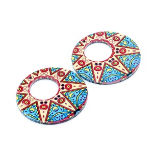 May include: Two round wooden earrings with a colourful geometric pattern in shades of red, yellow, blue, and white. The earrings have a large hole in the centre.