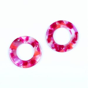 Op de afbeelding: Twee ronde, roze en witte marmerachtige plastic cirkels met een gat in het midden. De cirkels zijn ongeveer 2,5 cm in diameter.