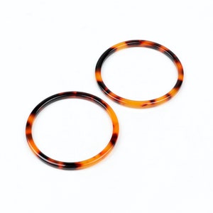 May include: Two brown and black tortoiseshell plastic rings. The rings are round and have a smooth finish.