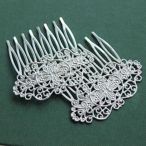 May include: Two silver hair combs with intricate filigree designs. Each comb features a central oval with a floral motif and delicate swirls.