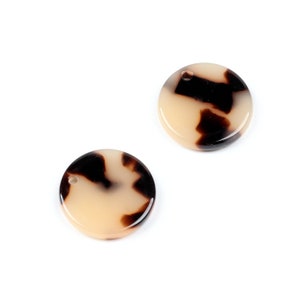 Puede incluir: Dos piezas redondas, de plástico, de color crema, decorativas con un patrón de carey marrón. Cada pieza tiene un pequeño agujero en la parte superior.