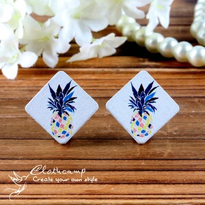 May include: A pair of white diamond-shaped earrings with a colorful pineapple design. The pineapple is yellow, pink, blue, and green.