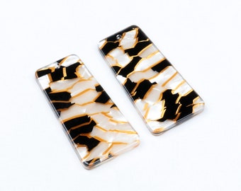May include: Two rectangular acrylic earrings with a black, white, and gold abstract pattern.
