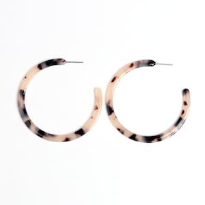 May include: A pair of large hoop earrings with a tortoiseshell pattern. The earrings are made of a light brown and black plastic material.