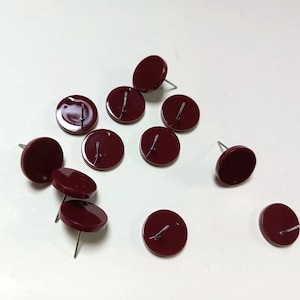 Könnte beinhalten: Zehn runde Ohrstecker in Marone mit silbernen Stiften. Die Ohrstecker sind auf einer weißen Oberfläche verstreut angeordnet.