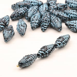 Może przedstawiać: Kolekcja niebieskich i czarnych szklanych koralików o fakturowanej powierzchni. Koraliki mają kształt łzy i mają metaliczny połysk.