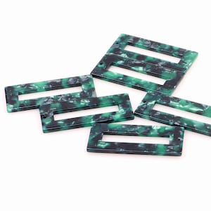 Peut inclure: Cinq pièces rectangulaires en plastique vert et noir avec un rectangle découpé au centre. Chaque pièce a un trou en haut.