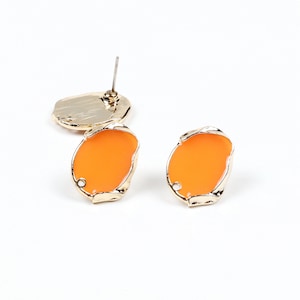 May include: A pair of orange and gold earrings. The earrings are oval shaped with a gold rim and a smooth orange center.