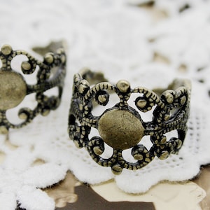 Puede incluir: Dos anillos de metal adornados de color dorado con un diseño circular. Los anillos tienen un patrón de filigrana y están hechos de un metal delicado.