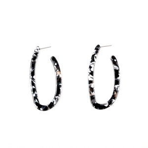 May include: A pair of black and white oval hoop earrings. The earrings are made of a marbled plastic material.