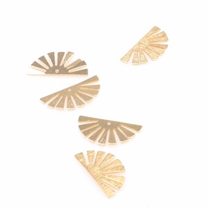 May include: Five gold metal sunburst shapes, each with a hole in the center. The shapes are scattered on a white background.