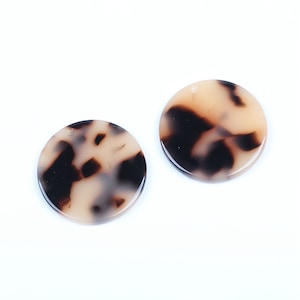 May include: Two round, cream-colored, resin earrings with a black and brown tortoiseshell pattern.