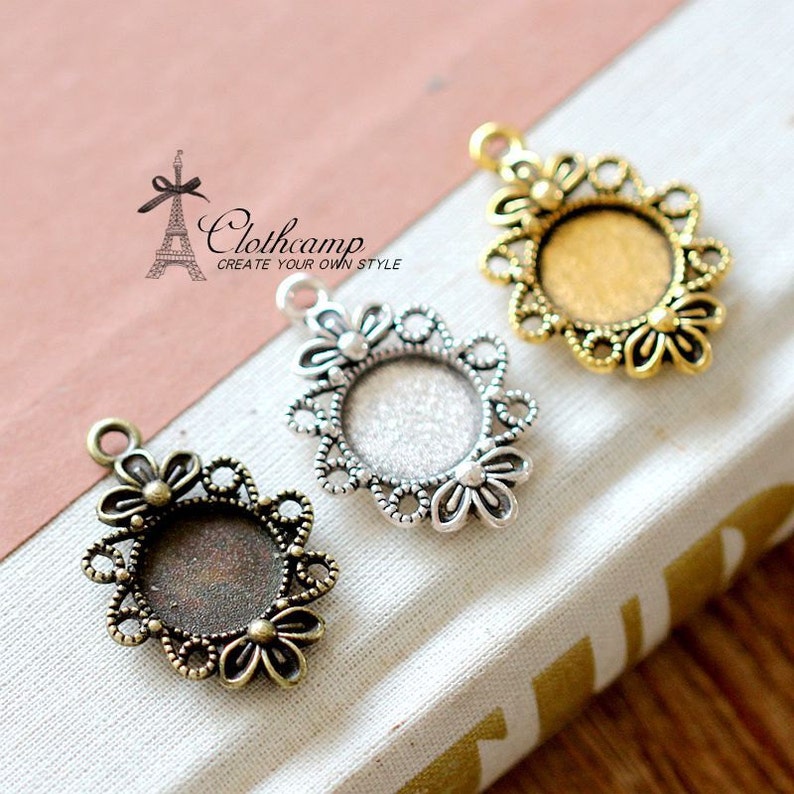 Puede incluir: Tres colgantes de plata, oro y bronce con un marco redondo abierto y un delicado dise&ntilde;o floral. Los colgantes tienen un bucle en la parte superior para sujetarlos a un collar o pulsera.