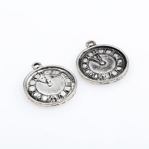 Può includere: Due ciondoli in argento a forma di quadrante dell'orologio con numeri romani. Le lancette dell'orologio sono impostate sulle 12.