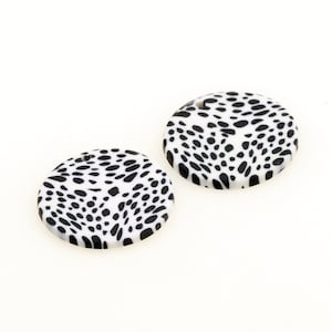 Pode incluir: Dois pingentes redondos de argila polimérica branca com um design de estampa animal em preto e branco. Cada pingente tem um pequeno furo para prender em um colar, pulseira ou outra joia.