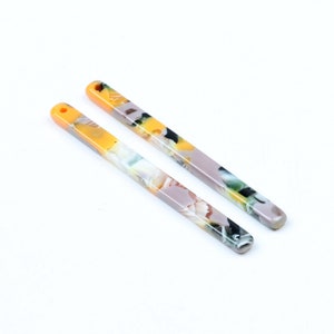 Könnte beinhalten: Zwei lange, dünne, gelbe und graue Haarsticks mit einem Blumenmuster.