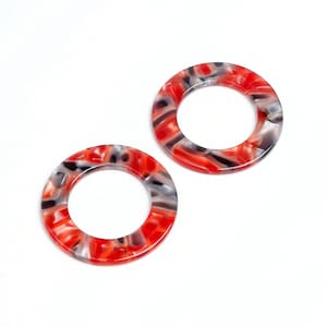 May include: Two plastic rings with a red, black and white patterned design. The rings are approximately 5 cm in diameter.
