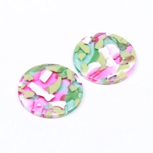 May include: Two round, colorful, green, pink, and white patterned resin cabochons.