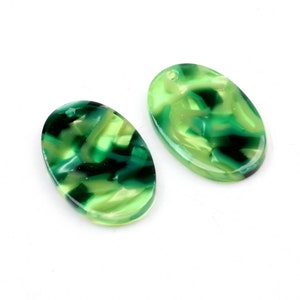 Op de afbeelding: Twee groene en witte ovale hars hangers met een swirl-patroon. De hangers hebben een gat aan de bovenkant om te rijgen.